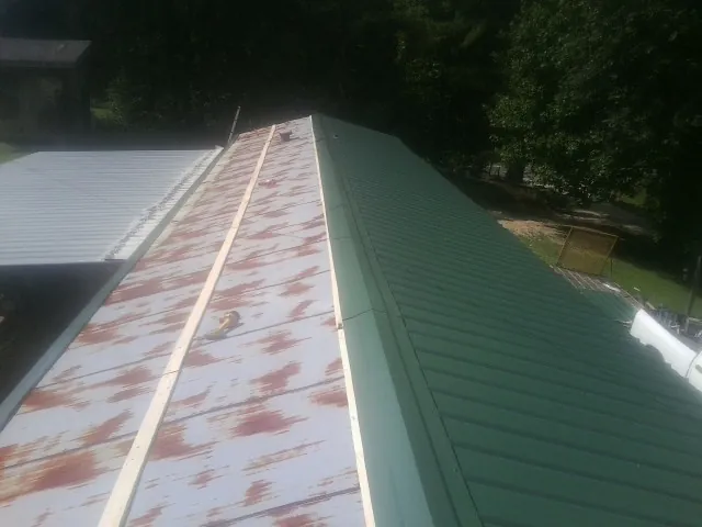 Old rusted panels beside newly installed green metal roofing — Wind Damage Roof Repair by Roofing Brothers in Alma